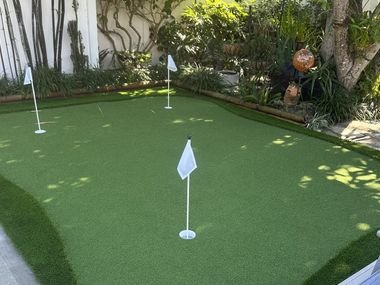 Putting green con tres banderas rodeado de bambú y plantas tropicales, junto a una tumbona.
