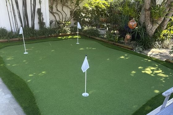 Putting green con tres banderas rodeado de bambú y plantas tropicales, junto a una tumbona.